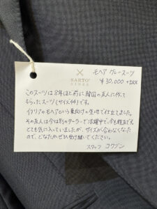 商品写真＆手書きタグ写真：上品なグレーのスーツと、「スタッフ コクブン」による手書きメッセージタグのアップ