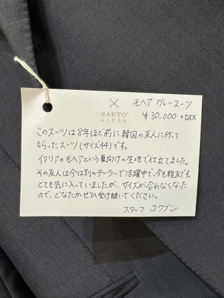 商品写真＆手書きタグ写真：上品なグレーのスーツと、「スタッフ コクブン」による手書きメッセージタグのアップ